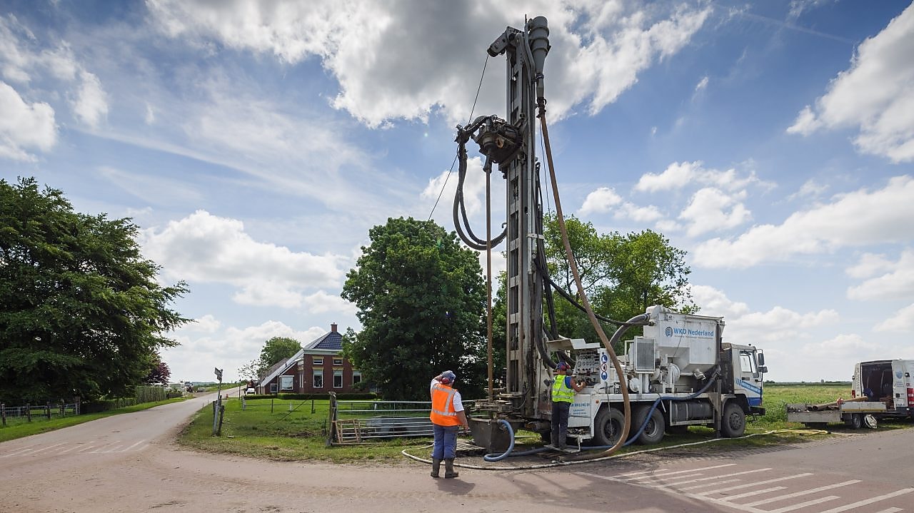 Man met oranje veiligheidsvest en vrachtwagen met boormaterieel
