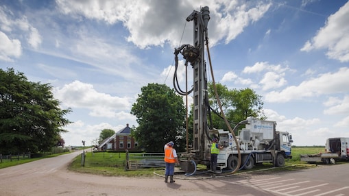 Man met oranje veiligheidsvest en vrachtwagen met boormaterieel