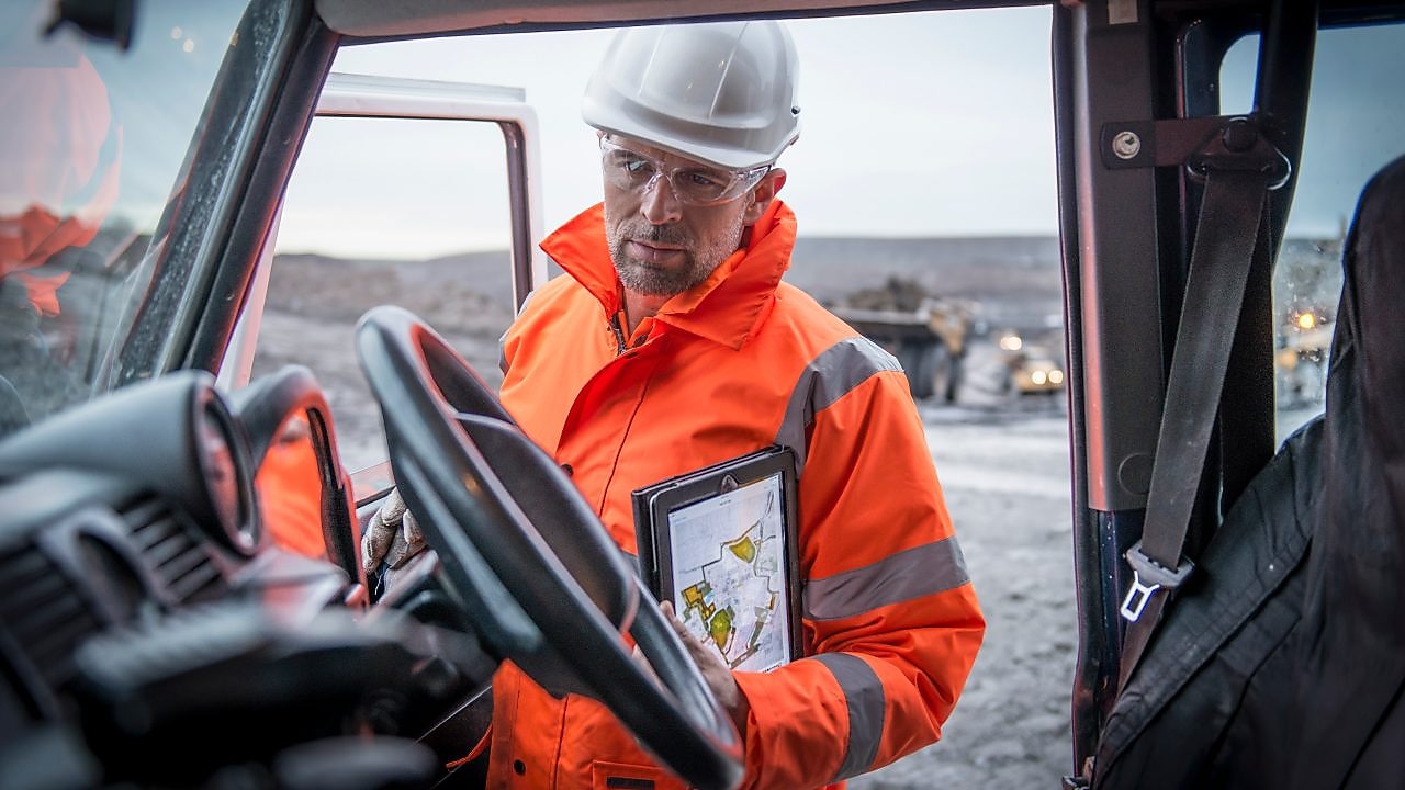 Medewerker in oranje overall met tablet onder arm gezien vanuit een auto