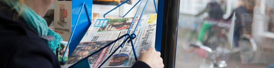 Een hand pakt de Telegraaf uit een rek