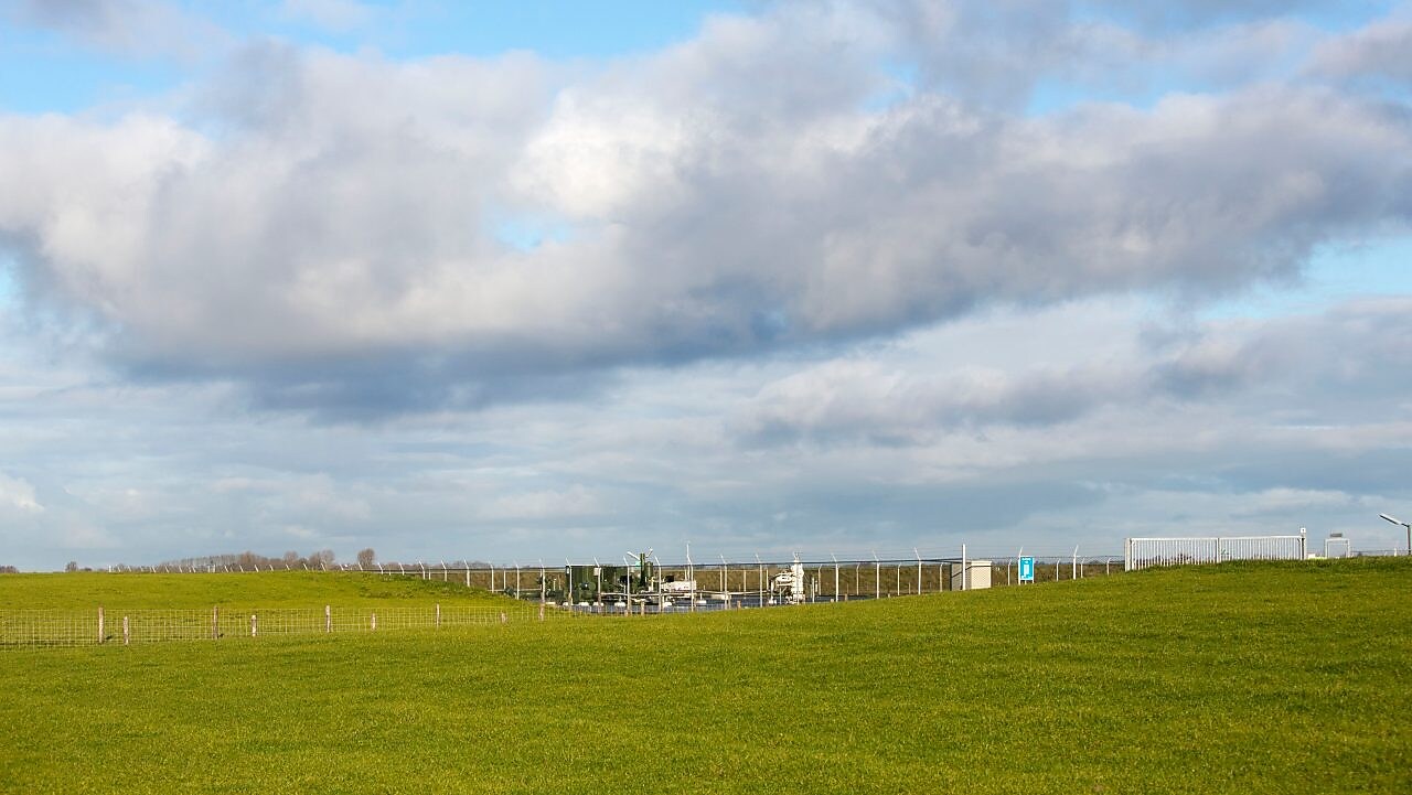 Groene weilanden met daarin een gaswinningslocatie onder een blauwe lucht