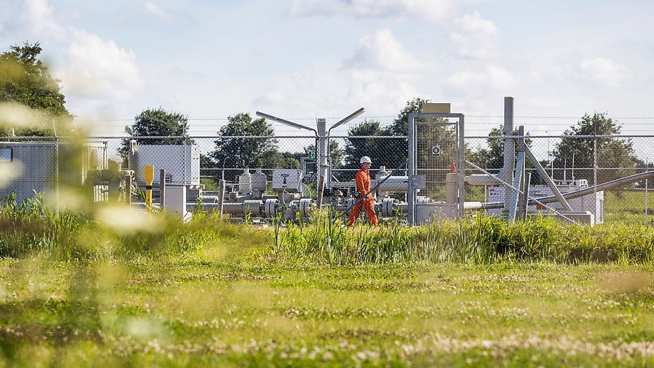 Man met oranje overall achter een hek