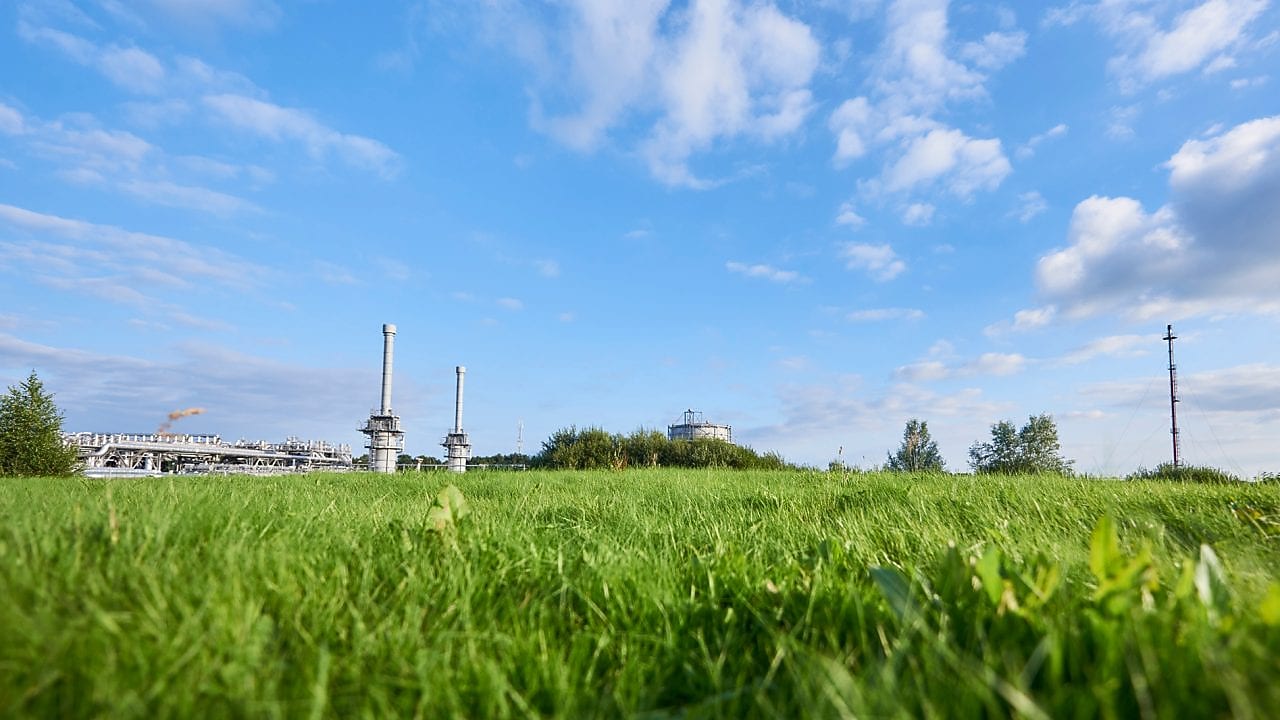 Blauwe lucht en groen gras met in de verte een gaswinningslocatie