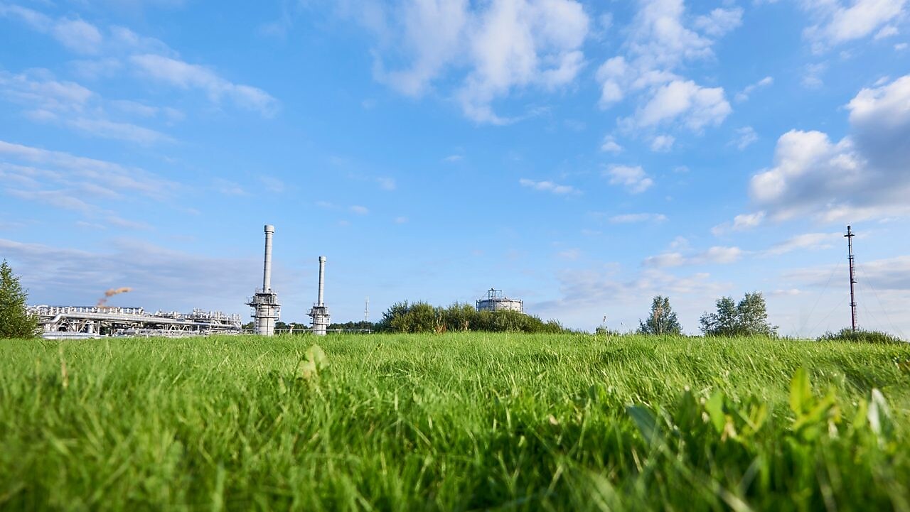 Blauwe lucht en groen gras met in de verte een gaswinningslocatie