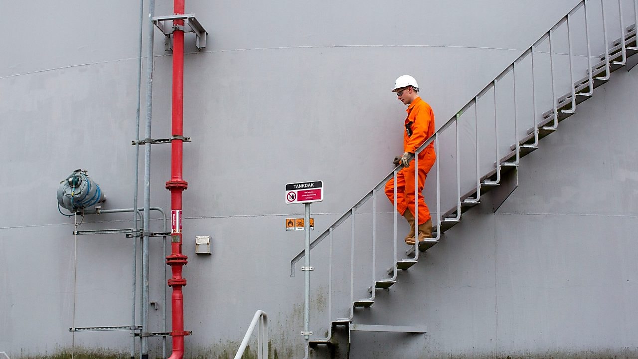 Medewerker in oranje overall loopt een ttrap af met zijn hand aan de leuning