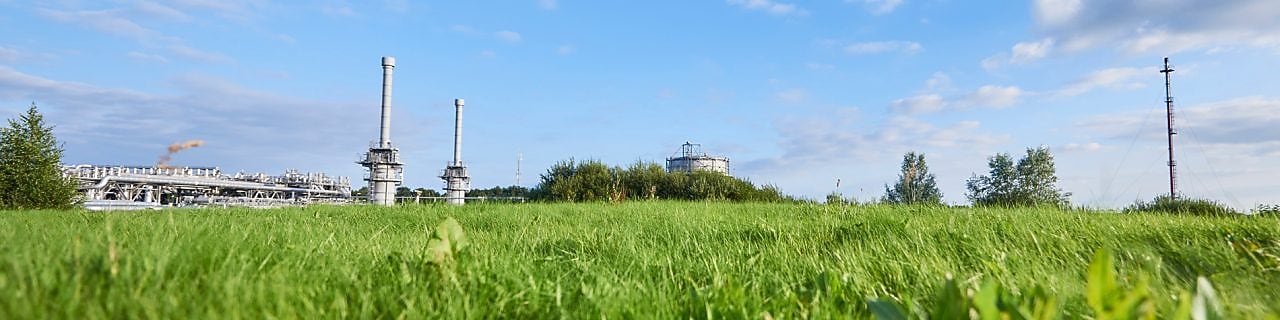 alt="Blauwe lucht en groen gras met in de verte een gaswinningslocatie"