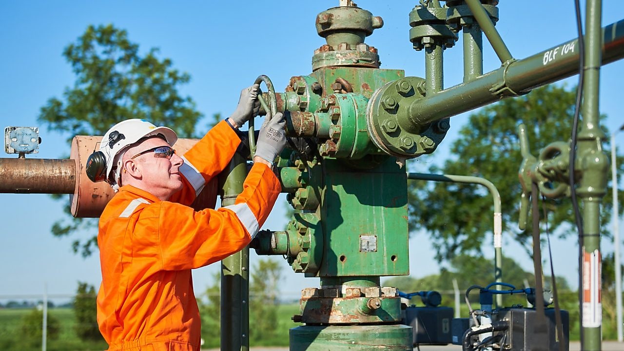 Man in oranje overall bedient een machine