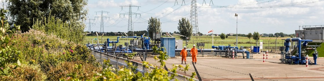 Twee mannen in oranje overalls lopen over een gaswinningsterrein