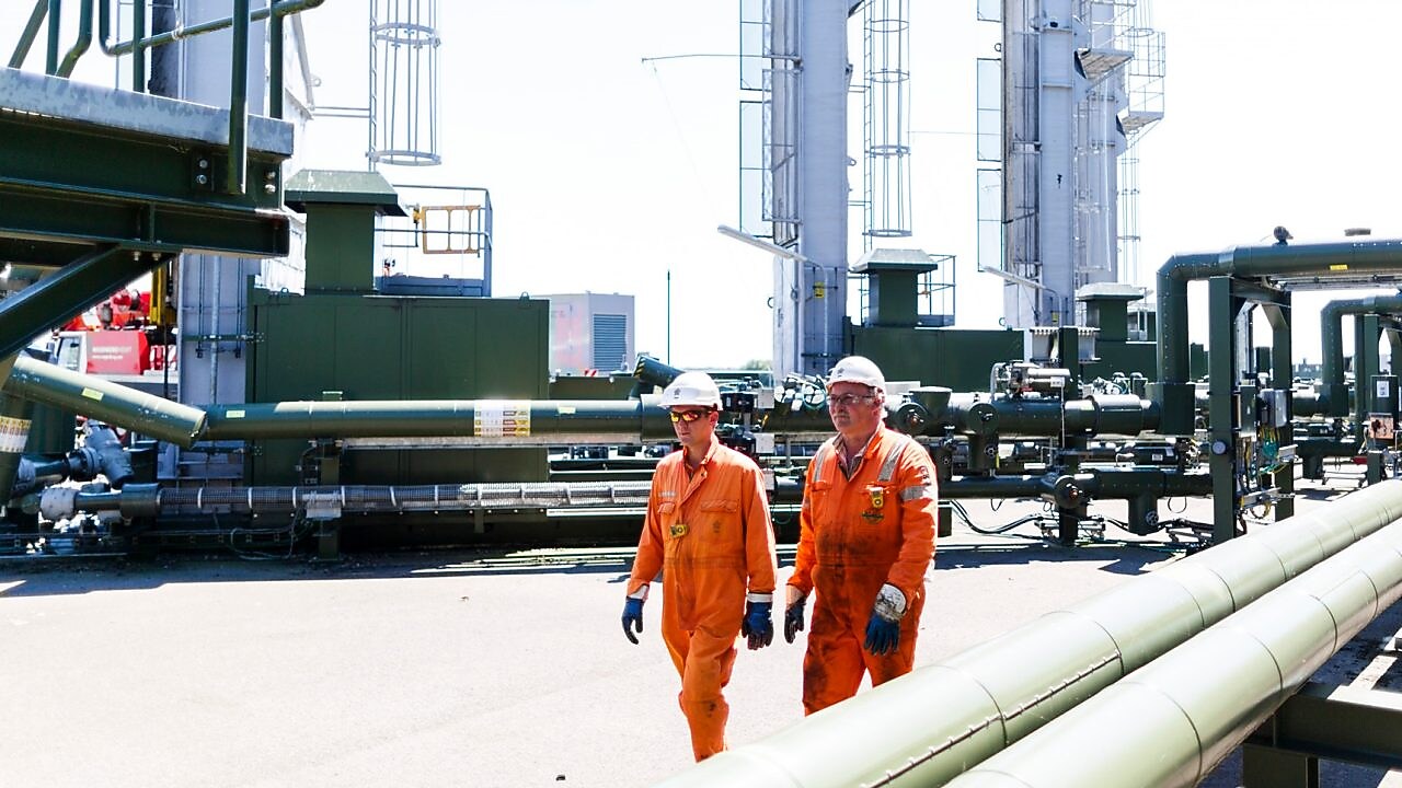 Twee mannen met oranje overall lopen over een winningslocatie