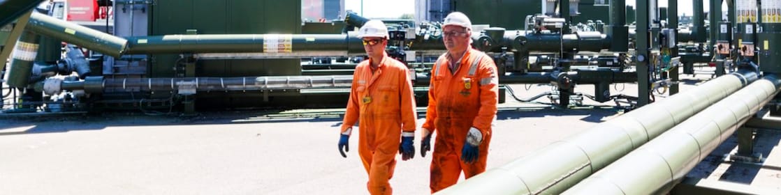 Twee mannen met oranje overall lopen over een winningslocatie