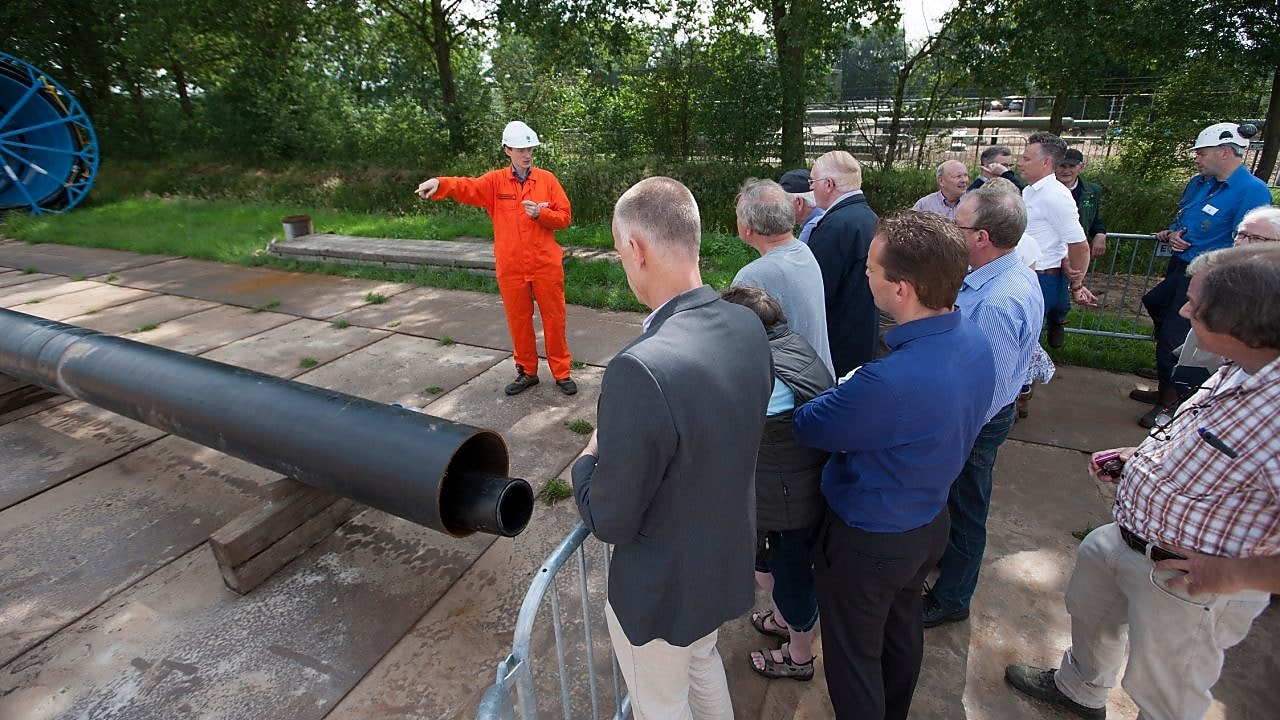 Man in oranje overall geeft uitleg aan groep toehoorders
