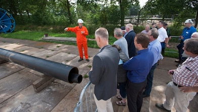 Man in oranje overall geeft uitleg aan groep toehoorders