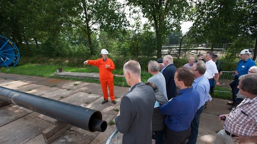 Man in oranje overall geeft uitleg aan groep toehoorders