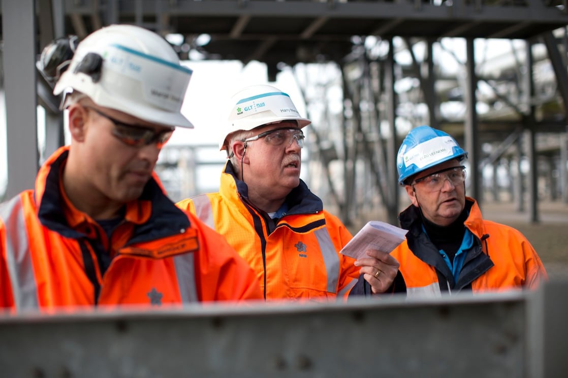 Medium foto van drie medewerkers in oranje jassen, met witte helmen en veiligheidsbrillen