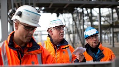 Medium foto van drie medewerkers in oranje jassen, met witte helmen en veiligheidsbrillen