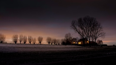 Winterlandschap in de schemer met kale bomen en een huis waarin lichtbrand