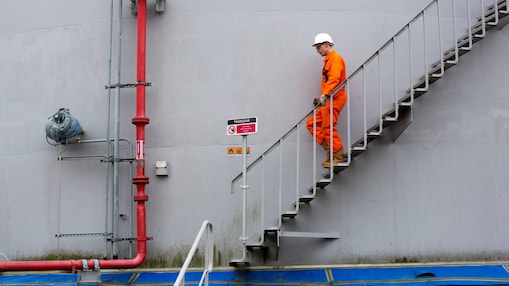 Medewerker in oranje overall loopt een ttrap af met zijn hand aan de leuning