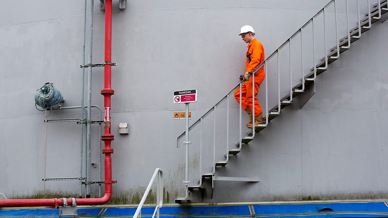 Medewerker in oranje overall loopt een ttrap af met zijn hand aan de leuning