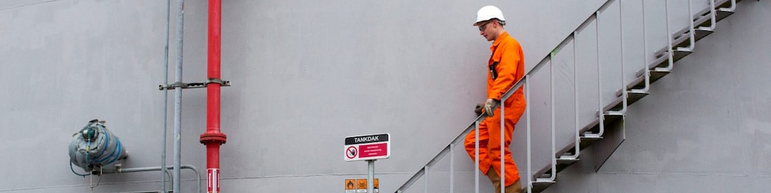 Medewerker in oranje overall loopt een ttrap af met zijn hand aan de leuning