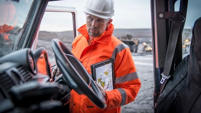 Medewerker in oranje overall met tablet onder arm gezien vanuit een auto