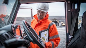 Medewerker in oranje overall met tablet onder arm gezien vanuit een auto