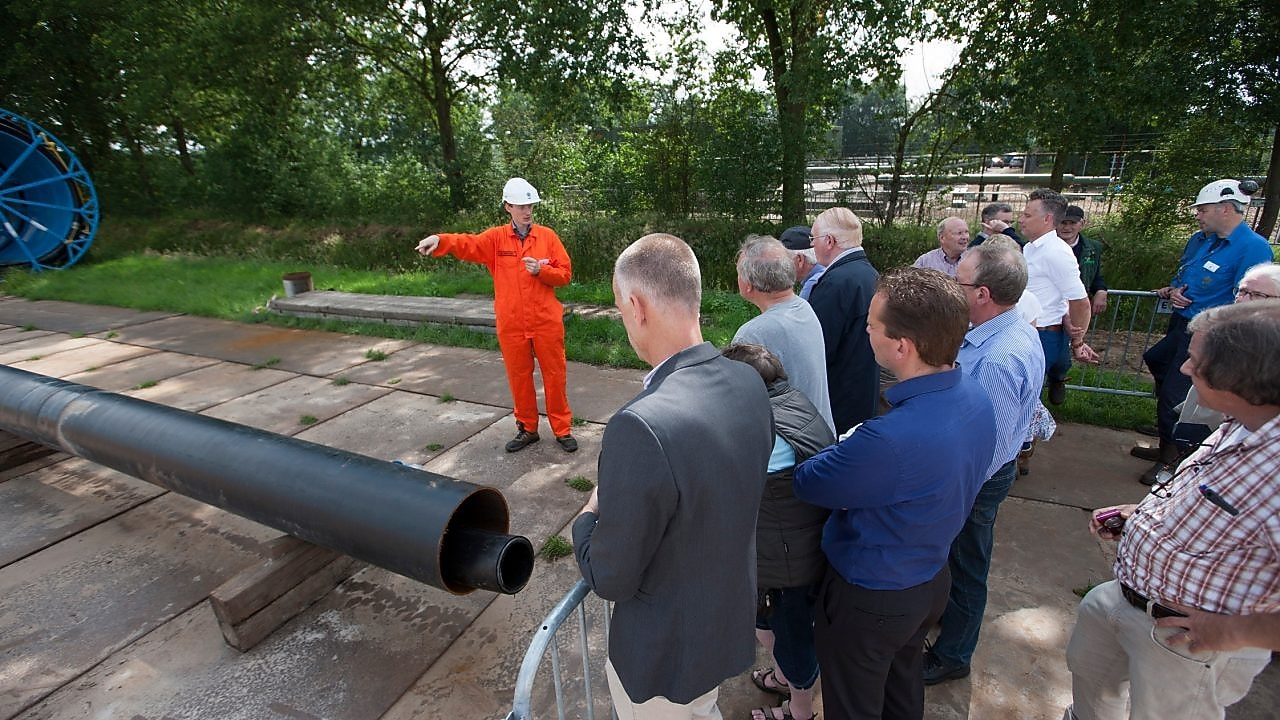 Man in oranje overall geeft uitleg aan groep toehoorders