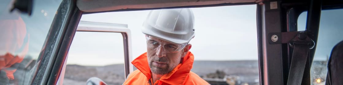 Medewerker in oranje overall met tablet onder arm gezien vanuit een auto