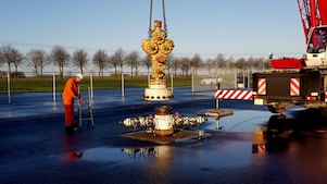 Medewerker in oranje overall bij kraan die gele afsluiter plaatst