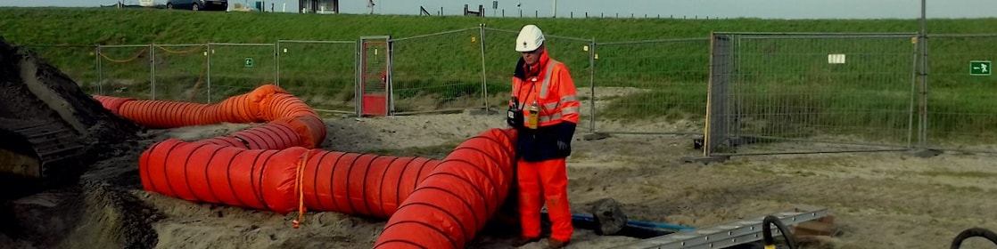 Medewerker in oranje overall met oranje stortbuis bij afgraving