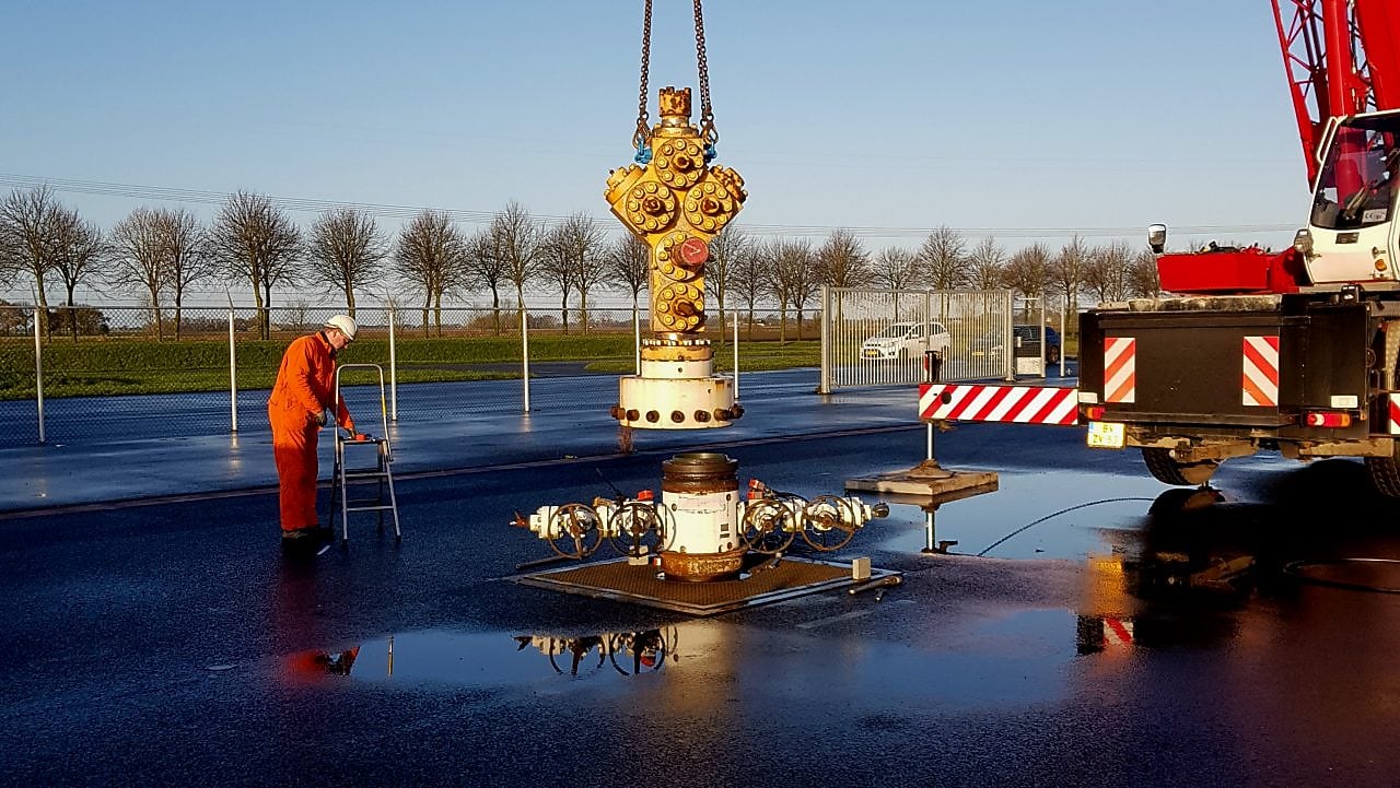 Medewerker in oranje overall bij kraan die gele afsluiter plaatst