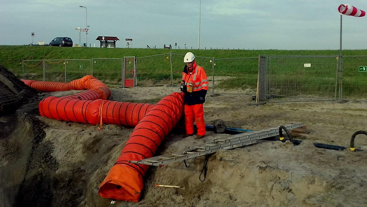 Medewerker in oranje overall met oranje stortbuis bij afgraving